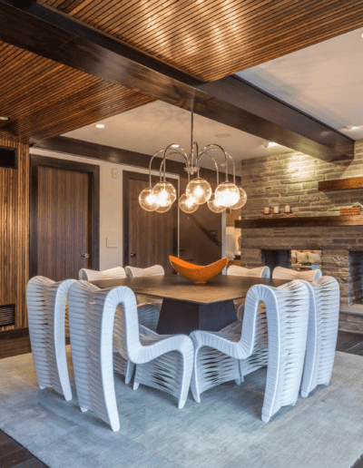 Modern dining room with wooden ceiling, stone fireplace, and unique white chairs.