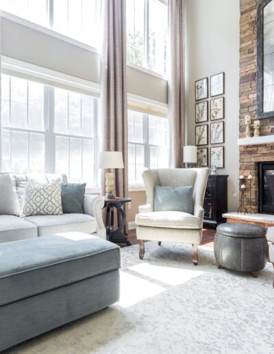 Bright and cozy living room with high ceilings, large windows, a stone fireplace, and elegant neutral-toned furnishings.