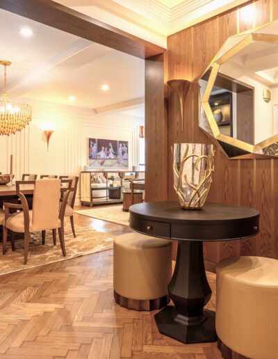 Elegant interior of a modern home featuring a herringbone floor with a round table and stools, a geometric mirror, and a view into a dining and living area.